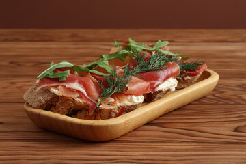 Buckwheat toasts with goat cheese, ham and arugula lying on a bamboo plate on a wooden table. Closeup