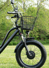 Front wheel side of the electric bicycle, view in sunny summer day in the  green grass. E bike motor with battery. Ecology and green energy concept. Ev – electric vehicle.