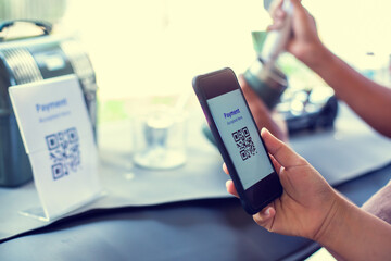 Customer hand using smart phone to scan Qr code payment tag  with blurry staff making coffee in cafe or restaurant.