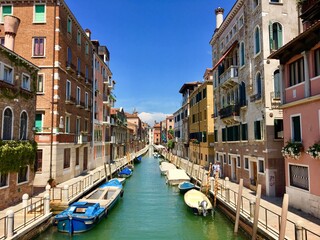 An incredible beautiful view of a canal in Venice, Italy on a bright summer day.  The canal is lined with boats and old colourful venetian homes.