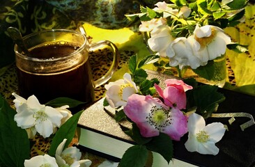 A cup of black coffee in a glass cup. Wooden pad, book and rose hips. Blurred foreground and background.