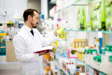 Happy man pharmacist checking assortment of drugs in pharmacy