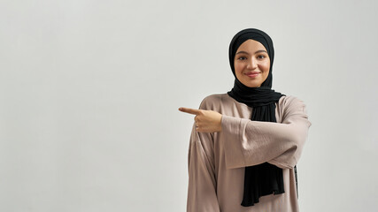 Happy young arabian woman in hijab pointing to side