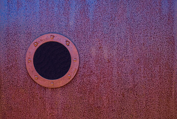 Porthole in a red rusty stel wall.