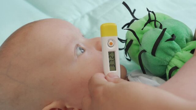 Mother taking baby temperature with digital thermometer, measuring armpit temp of a three month old baby boy, rising temperature on thermometer display. High quality 4k footage