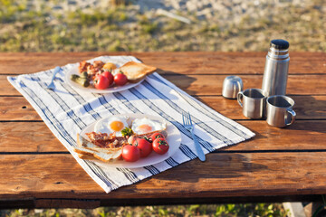 Breakfast in nature. Fried eggs with bacon, fried toast and hot coffee from a thermos
