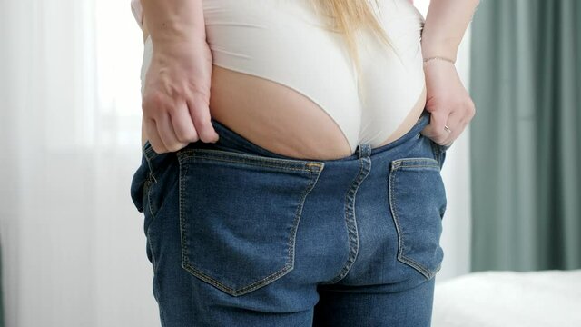 Young woman with big bottom and wide hips pulling and fitting in tight jeans. Concept of excessive weight, obese female, dieting and overweight problems