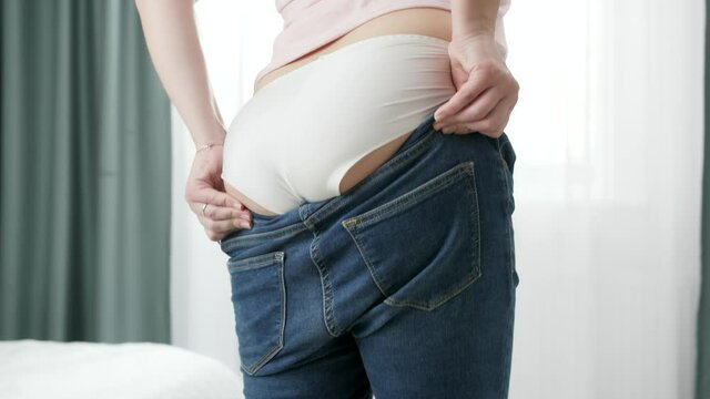 Young obese woman with big thighs and wide hips pulling tight jeans on bottom. Concept of excessive weight, obese female, dieting and overweight problems