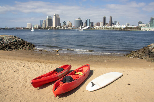 Two kayaks and a paddle board by a launching ramp in Coronado with view of of Downtown San Diego skyline across the bay. California, USA.