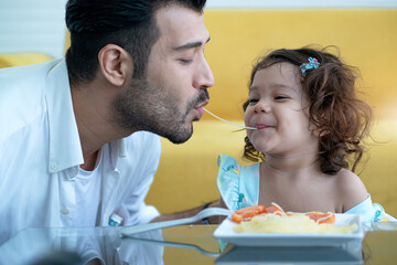 Cute little girl enjoying on the same string of Spaghetti pasta as her father eats, Father's day concept