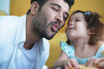 Cute little girl enjoying on the same string of Spaghetti pasta as her father eats, Father's day...