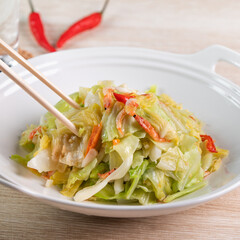 Stir-fried cabbage with sergestid Sakura shrimp in white plate on wooden table background.
