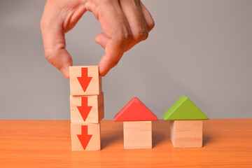 Toy house and red arrow down on wooden blocks. Reducing demand for home buying and low cost real estate concept.
