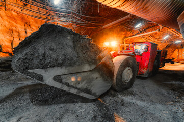 An underground loading machine carries a full bucket of ore. Special low-profile equipment for...