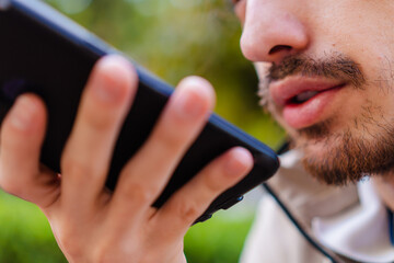 close up of a man sending an audio message on his smart cell phone outside in a city park
