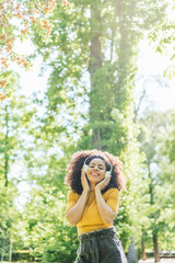 Pretty afro woman listens to music with headphones in a garden.