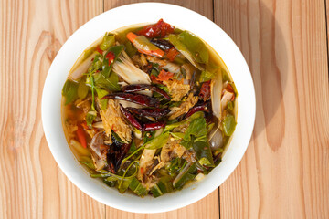 Sour and Spicy Smoked Dry Fish Soup in a white ceramic plate on a wooden table . Tom Klong IN Thai. Thai Food.