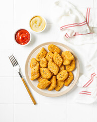 Chicken nuggets in a plate, ketchup and cheese sauce on a light background. Fast food top view