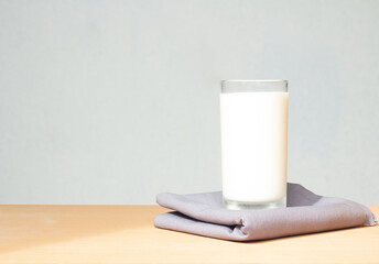 Pure milk drinks in clear glass are naturally healthy foods placed on a gray cloth on a on a morning sun light wiht blue background and copy space for text.