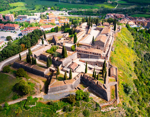 Fototapeta premium Scenic aerial view of medieval walled Castle on hilltop on background of small Spanish village of Hostalric in green spring valley, Girona, Catalonia.