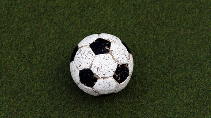 Old Soccer or football ball with paint peeling off on artificial green grass background
