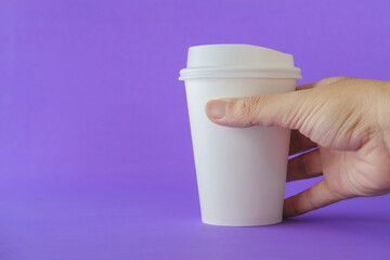 Close up of Man Hand Holding a White Paper Coffee Cup on a Purple Background.