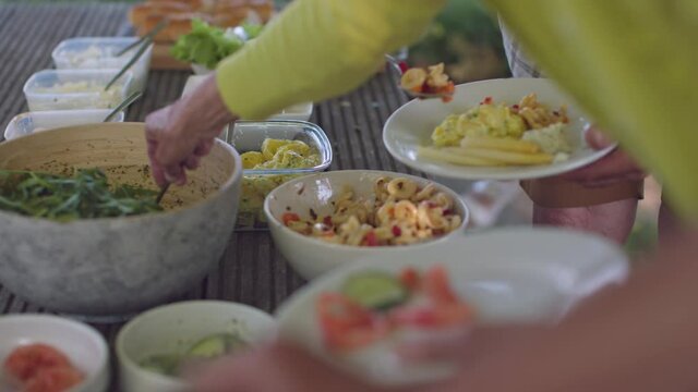 point of view from a party or restaurant or cafe table - hands fill the plates with food at the buffet - outdoor scene in slow motion