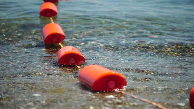 Orange safety buoys on a rope floating in the sea on a sunny day, close up. Fencing of the swimming area on the beach.
