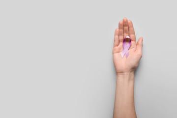 Fototapeta na wymiar Female hand with lilac ribbon on light background. Cancer awareness concept
