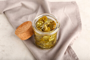 Glass jar with canned jalapeno on light background
