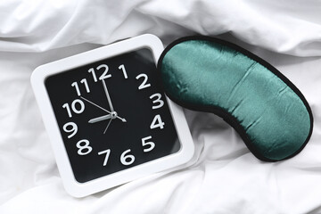 Stylish clock and sleeping mask on bed