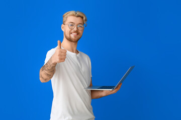 Fototapeta na wymiar Handsome man with laptop showing thumb-up on color background