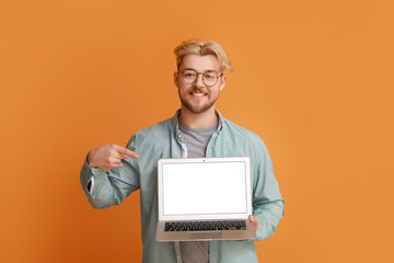 Handsome man pointing at laptop on color background