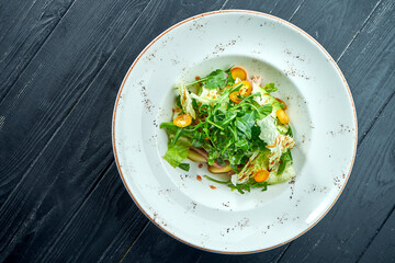 Appetizing, dietary salad with arugula, sauce, lettuce and warm beef in a white plate on a dark wood background. Healthy food