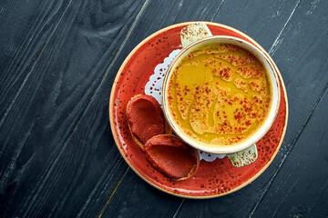 Traditional Moroccan soup - Harira, yellow lentil soup with cilantro in a red plate on a black wood...