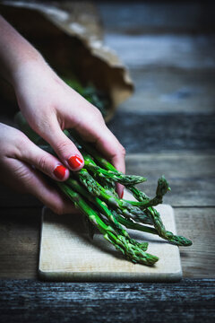 Women�s hands put green asparagus on a cutting board