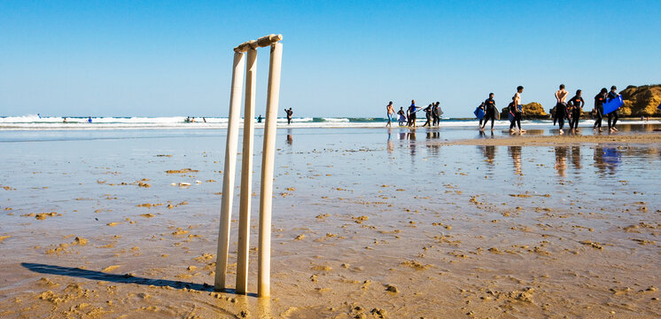 Cricket stumps on a beach with surfers in background