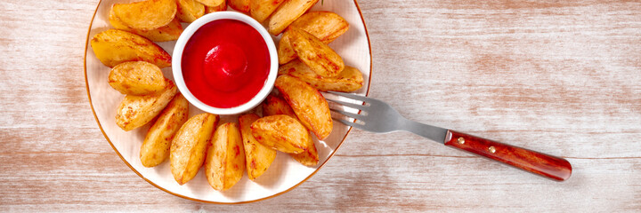 Baked potato wedges panorama with a fork, shot from above on a rustic background