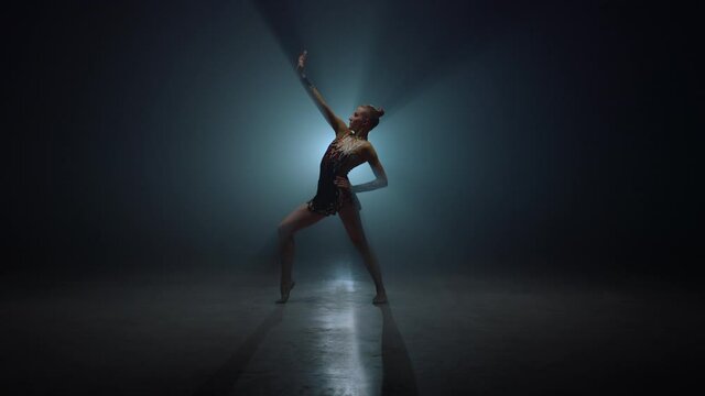 Graceful sportswoman posing indoors. Slim gymnast bending in dark space.