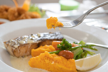 Cutlery is scooping pumpkin puree in dish salmon steak on the dining table in the restaurant.
