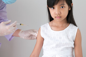 Female doctor or public health worker is injecting a flu treatment or a coronavirus or COVID-19 vaccine into the arm of an Asian child girl.