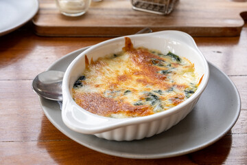 Baked spinach with cheese in a white bowl on the dining table