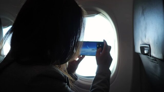 Unrecognizable woman photographs the view from the airplane window on the phone.