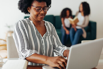 Mature woman working on laptop with family in background
