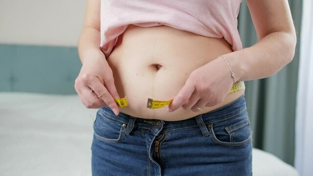 Young obese woman struggling to measure big belly with measuring tape. Concept of excessive weight, obese female, dieting and overweight problems