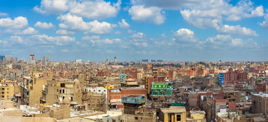 Panorama of shabby buildings with satellite dishes on rooftops against blue cloudy sky in ancient...