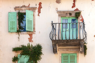 Facade of old shabby building with green shutters and balcony