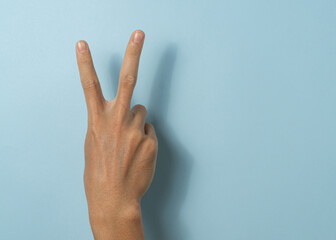 Hand a man show peace sign on blue background with a copy space.