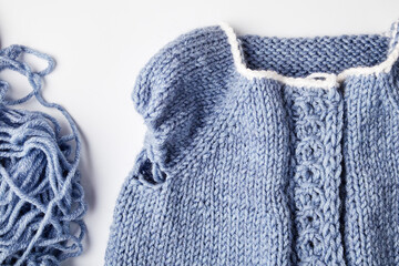 blue knitted product on knitting needles on a white background