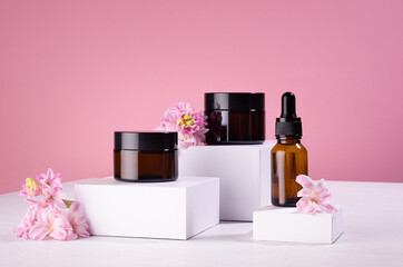 Cosmetic mockup -  jars for cream, essential oil bottle of amber glass on white podiums with pink...
